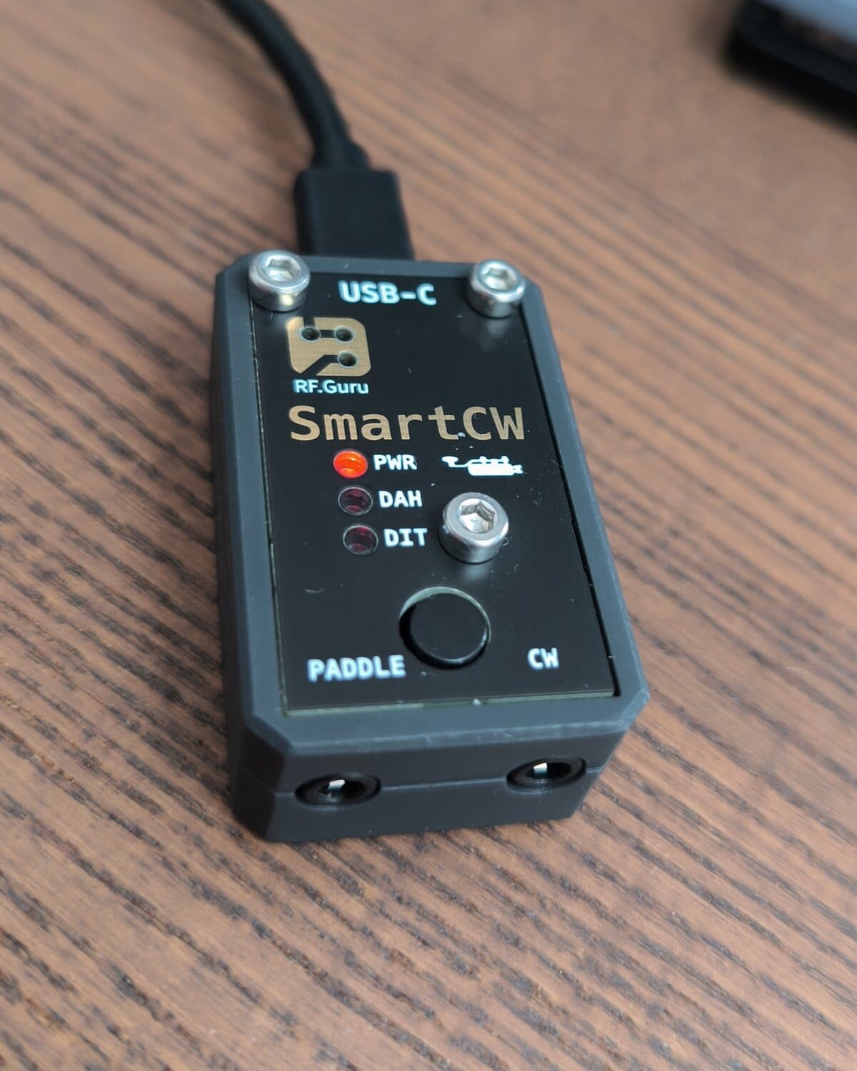 SmartCW close up: USB-C on top, the RF.Guru mark, the SmartCW name, the PWR, DAH and DIT LEDs, the PTT button, and the PADDLE and CW jacks on the front edge