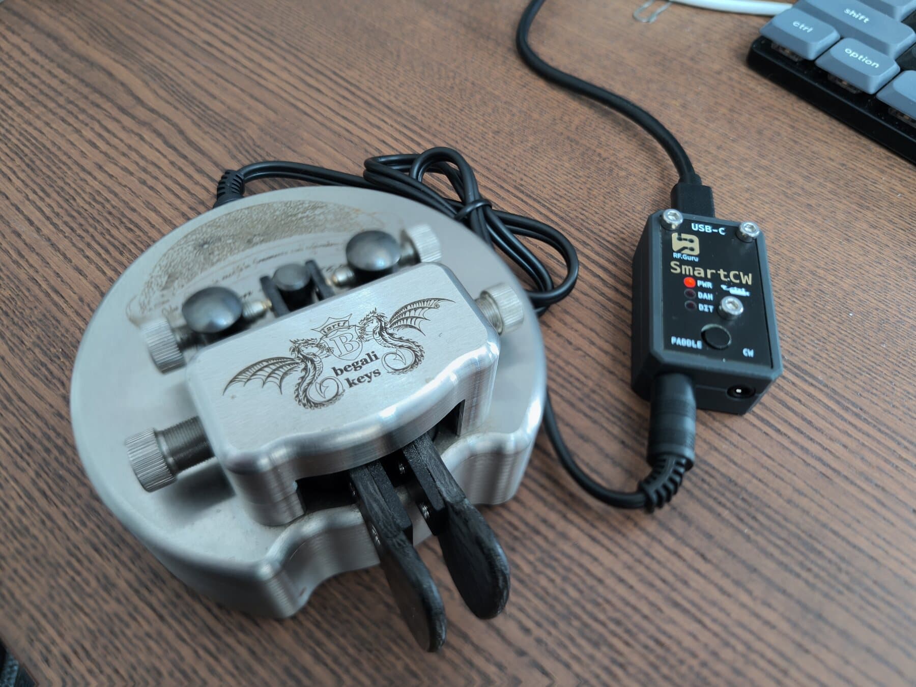 SmartCW, a small black box with PWR, DAH and DIT LEDs, a PTT button and PADDLE and CW jacks, wired to an iambic paddle and to a computer over USB-C